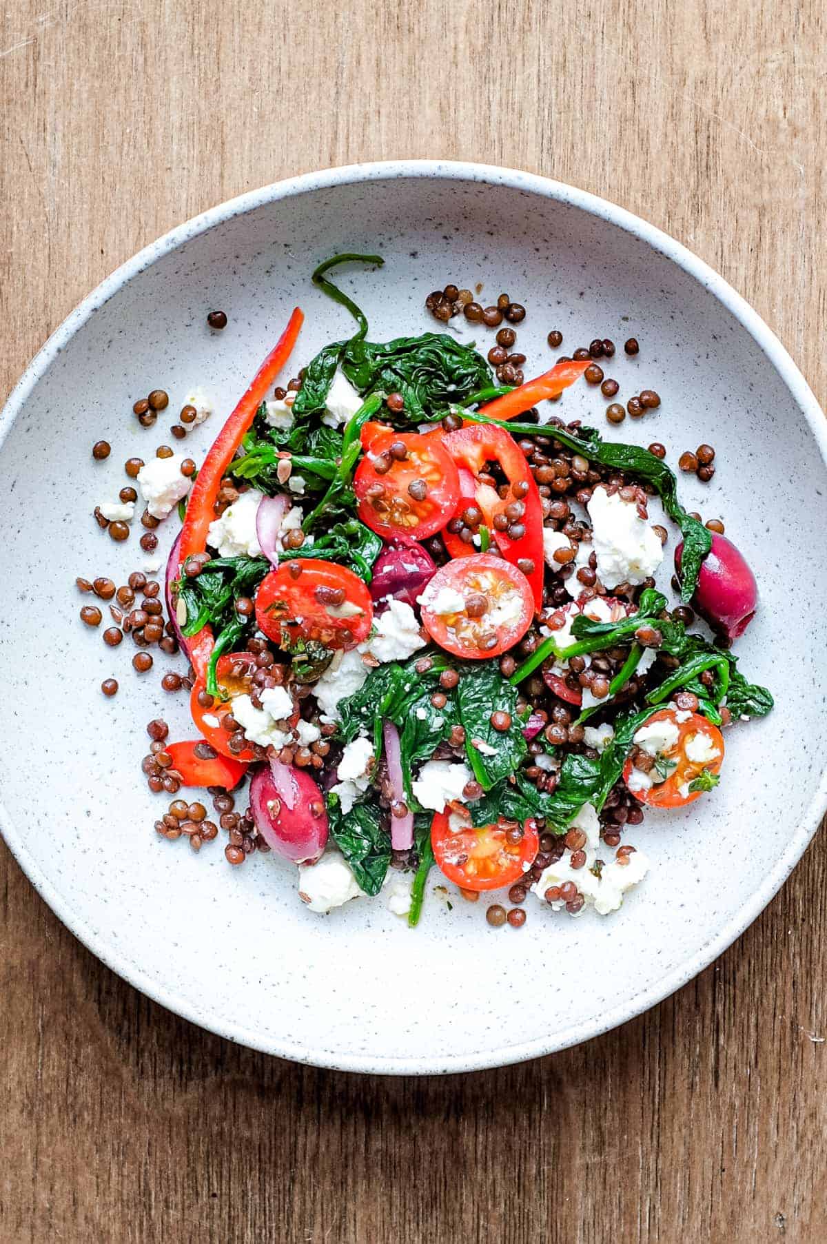 A bowl of Greek lentil salad featuring tomatoes, spinach, lentils, feta and red onion