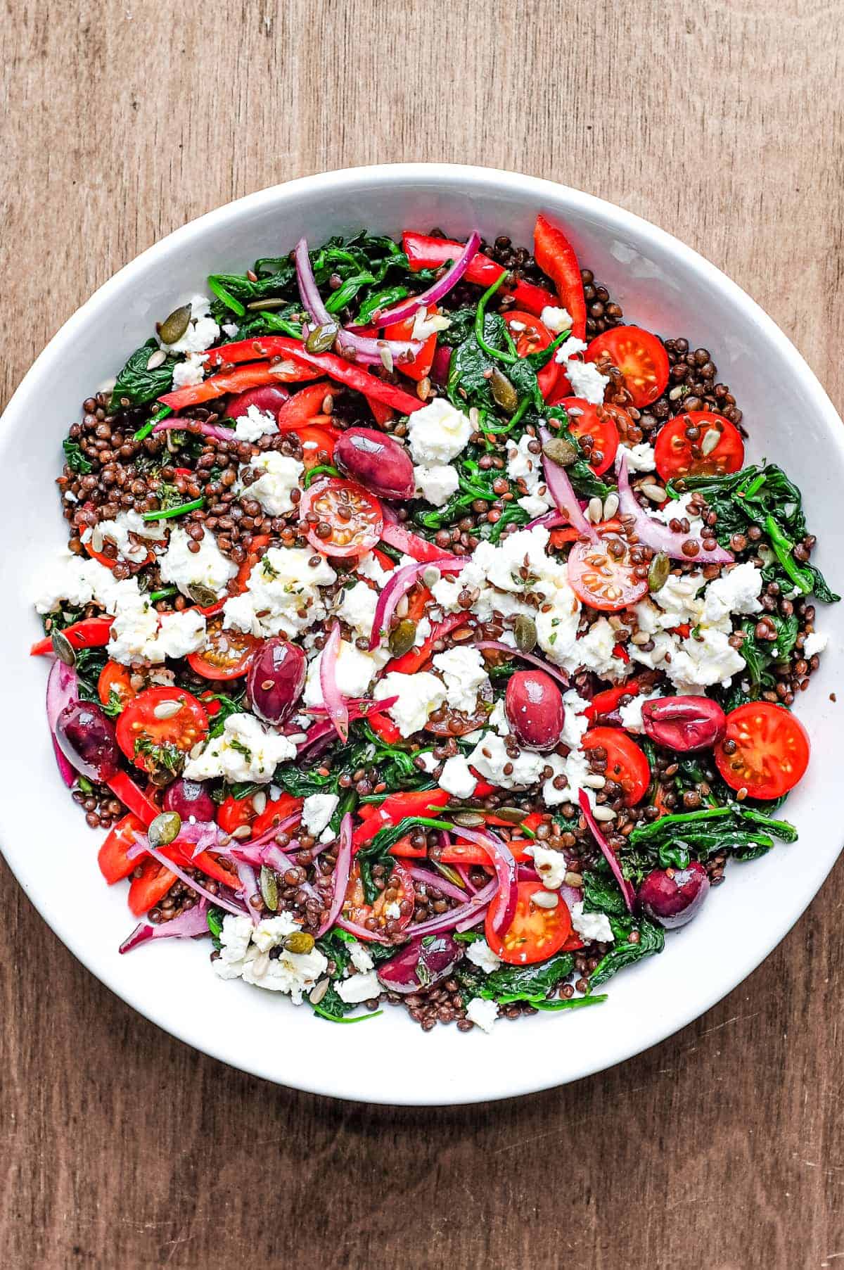 A bowl of Greek lentil salad featuring tomatoes, spinach, lentils, feta and red onion