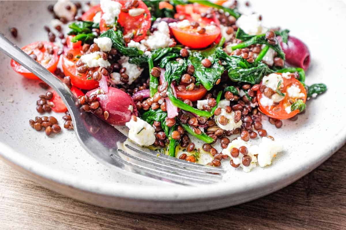 A bowl of Greek lentil salad featuring tomatoes, spinach, lentils, feta and red onion