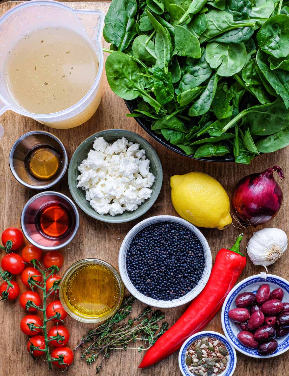 Ingredients for a Greek lentil salad: lentils, spinach, garlic, feta, tomato, pepper, olives, onion, lemon, vinegar and olive oil