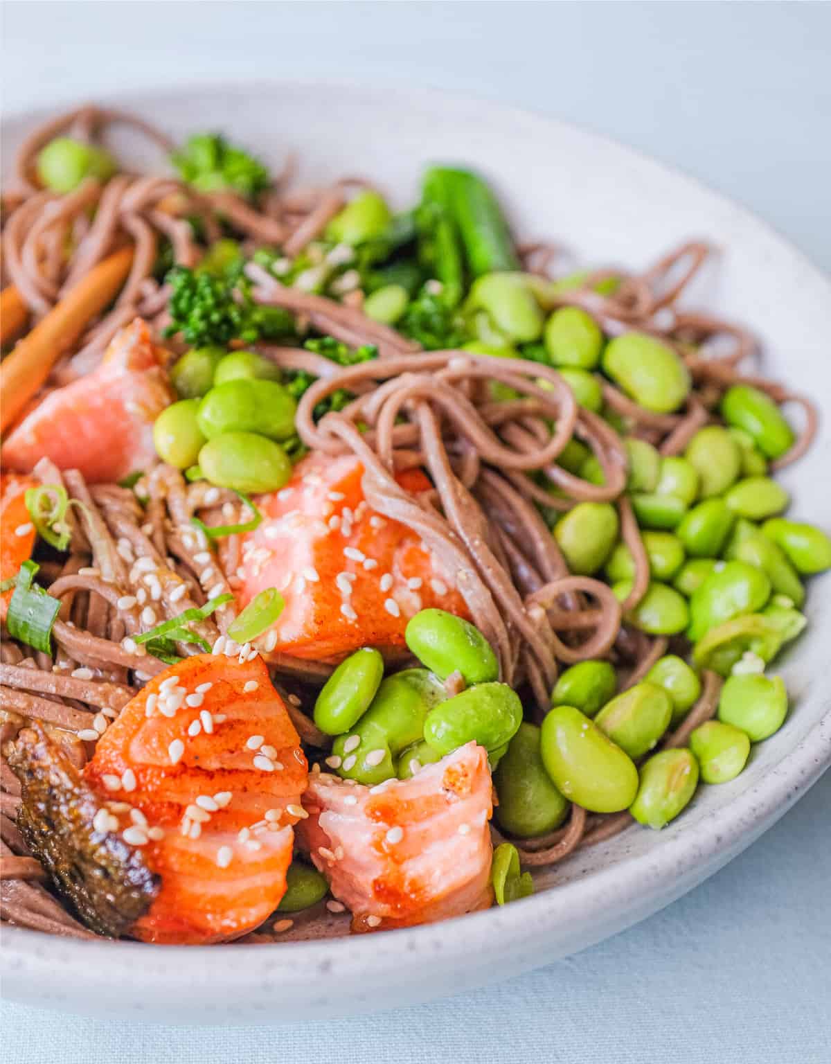 A bowl of salmon with soba noodles with broccolini and edamame.