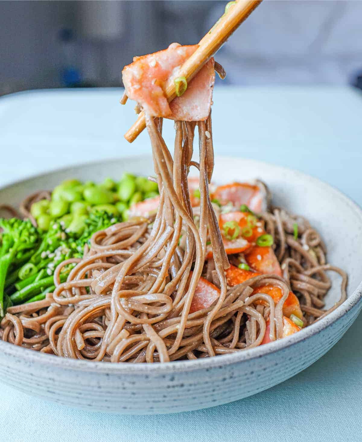 Chopsticks holding some salmon and soba noodles