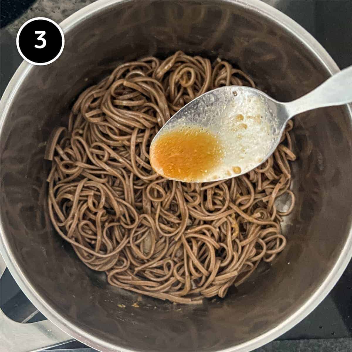 Soba noodles in a small pan being dressed in a miso dressing 