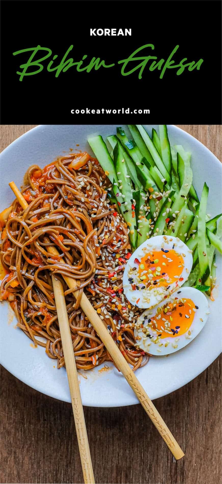 A bowl of Asian noodles called Bibim Guksu. Garnished with eggs and cucumber. Chopsticks are wrapped in the noodles.
