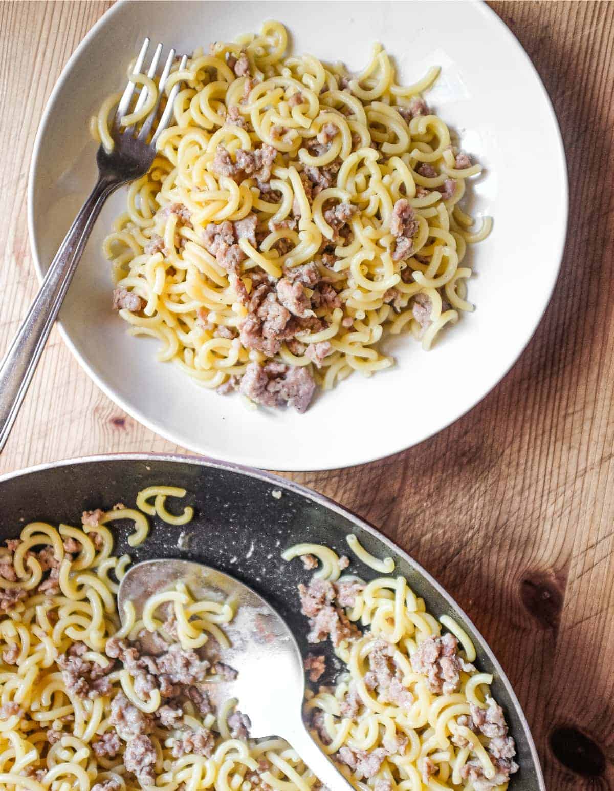 A bowl of Gramigna pasta with sausage sits next to a pan full of the pasta