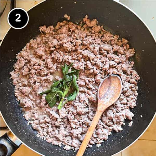 Sausage meat frying in a pan with sage