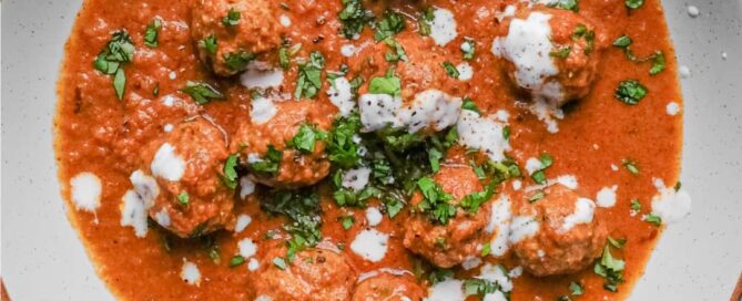 A bowl of Kofta (meatball) curry drizzled with yoghurt and garnished with chopped cilantro