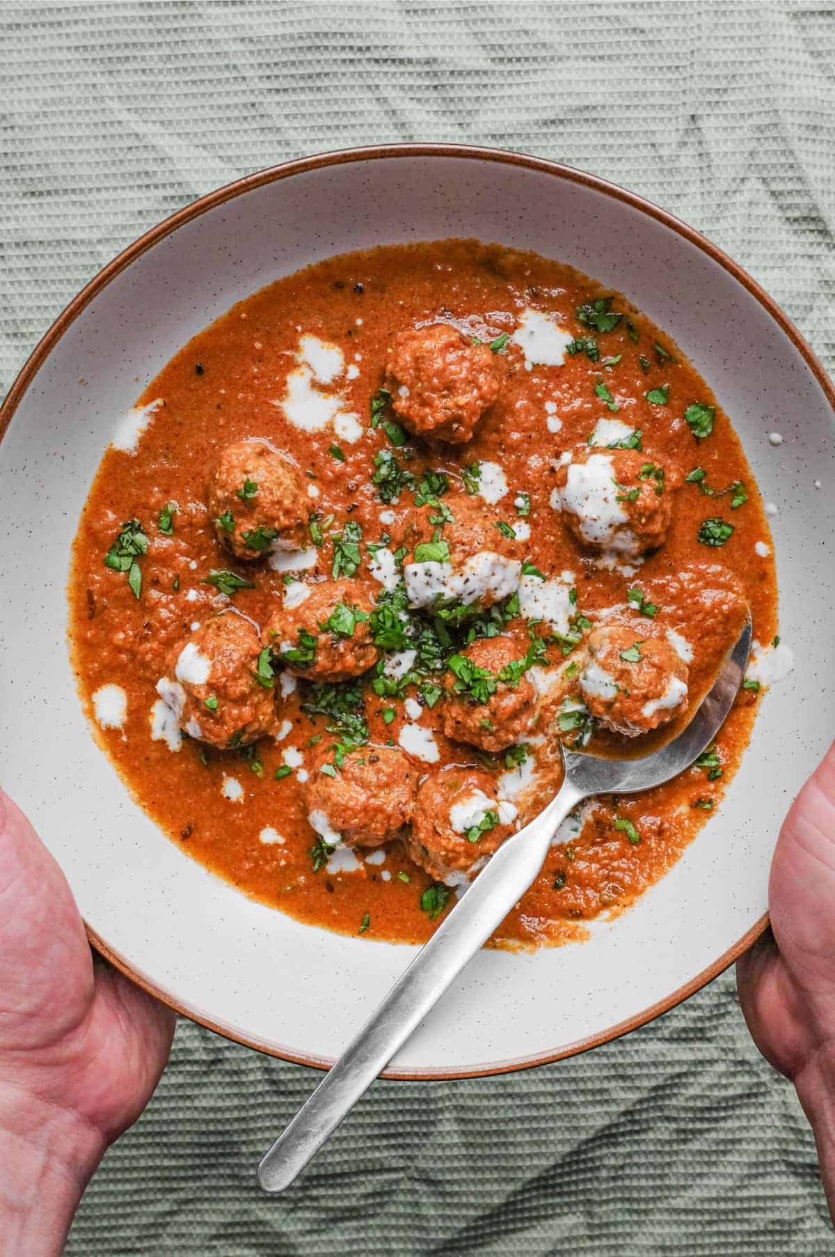 A bowl of Kofta (meatball) curry drizzled with yoghurt and garnished with chopped cilantro