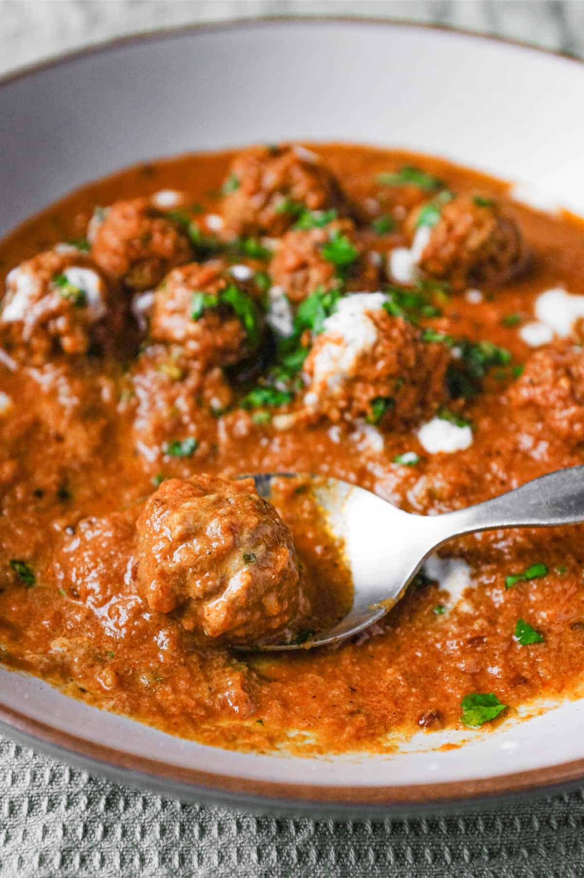 A bowl of Kofta (meatball) curry drizzled with yoghurt and garnished with chopped cilantro