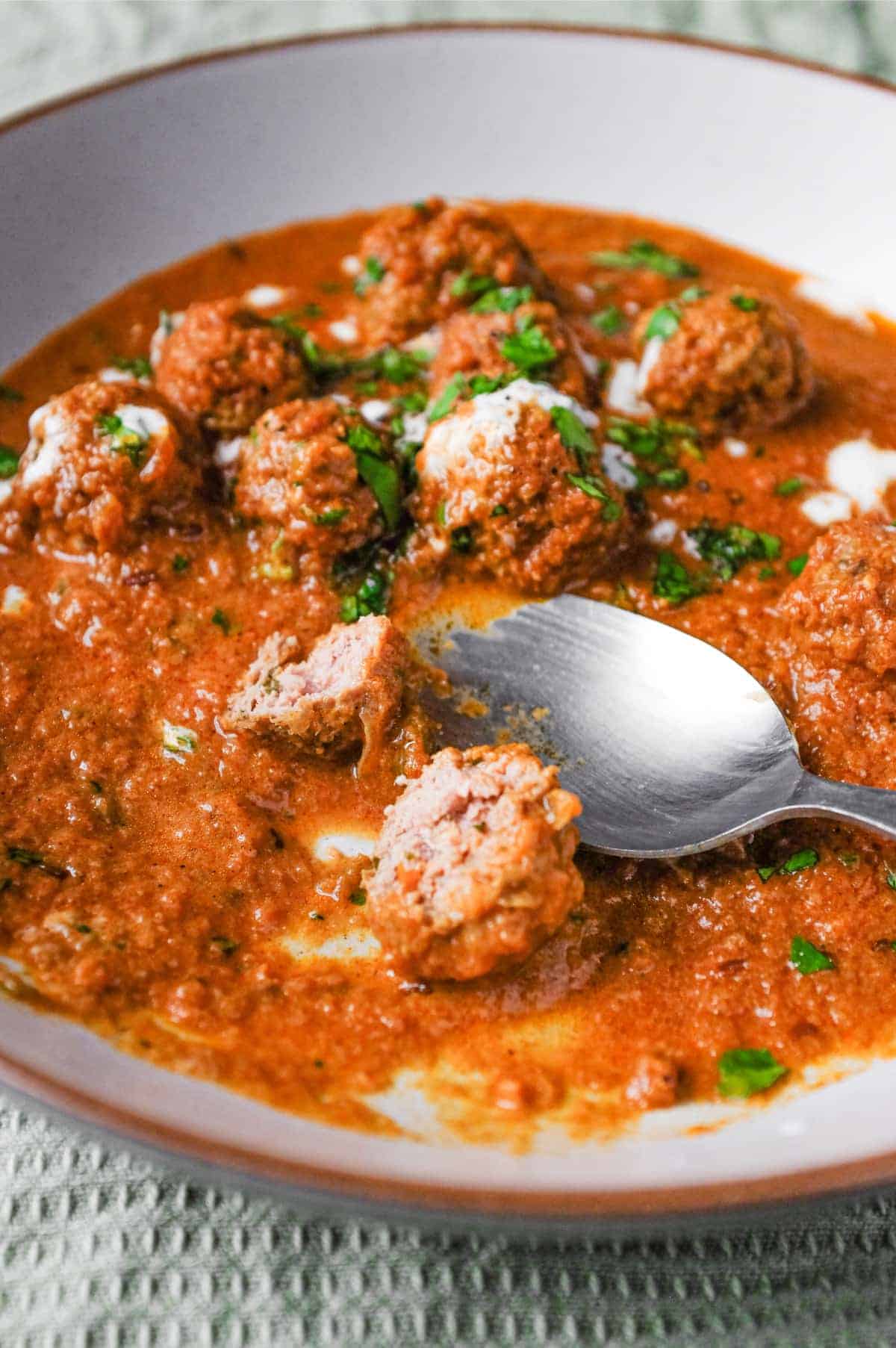 A bowl of Kofta (meatball) curry drizzled with yoghurt and garnished with chopped cilantro