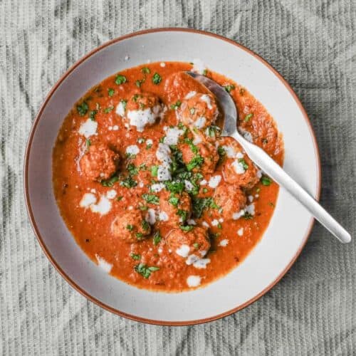 A bowl of Kofta (meatball) curry drizzled with yoghurt and garnished with chopped cilantro