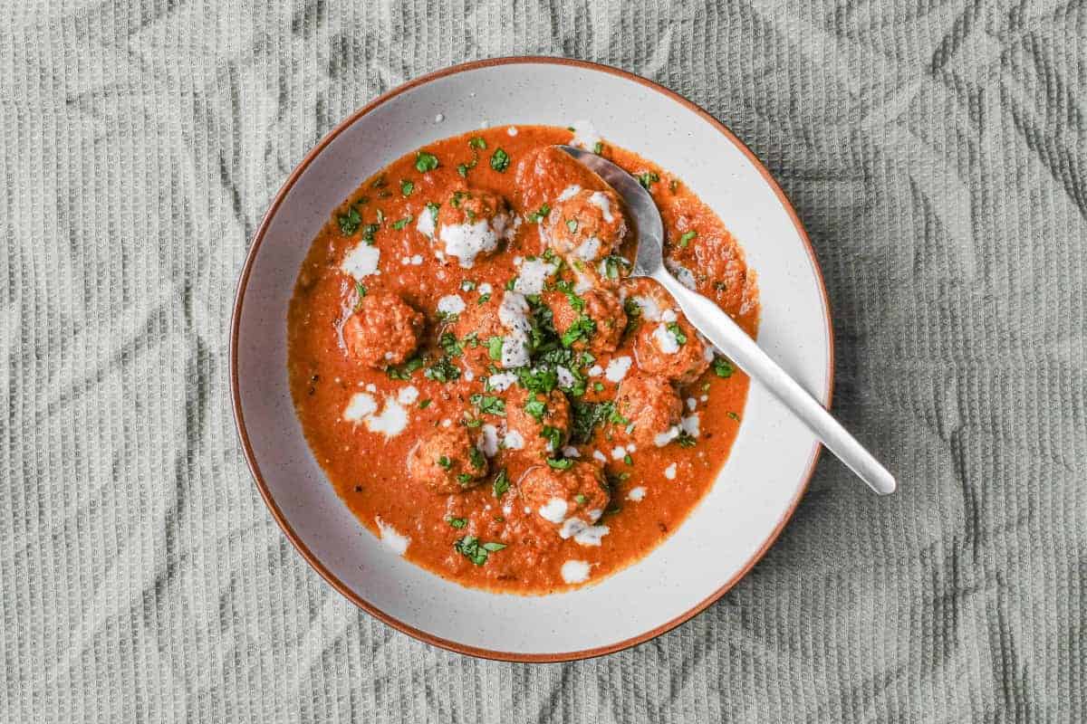 A bowl of Kofta (meatball) curry drizzled with yoghurt and garnished with chopped cilantro