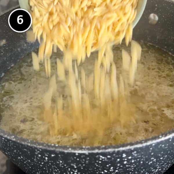 A small bowl of orzo pasta is poured into a pan of bubbling soup.