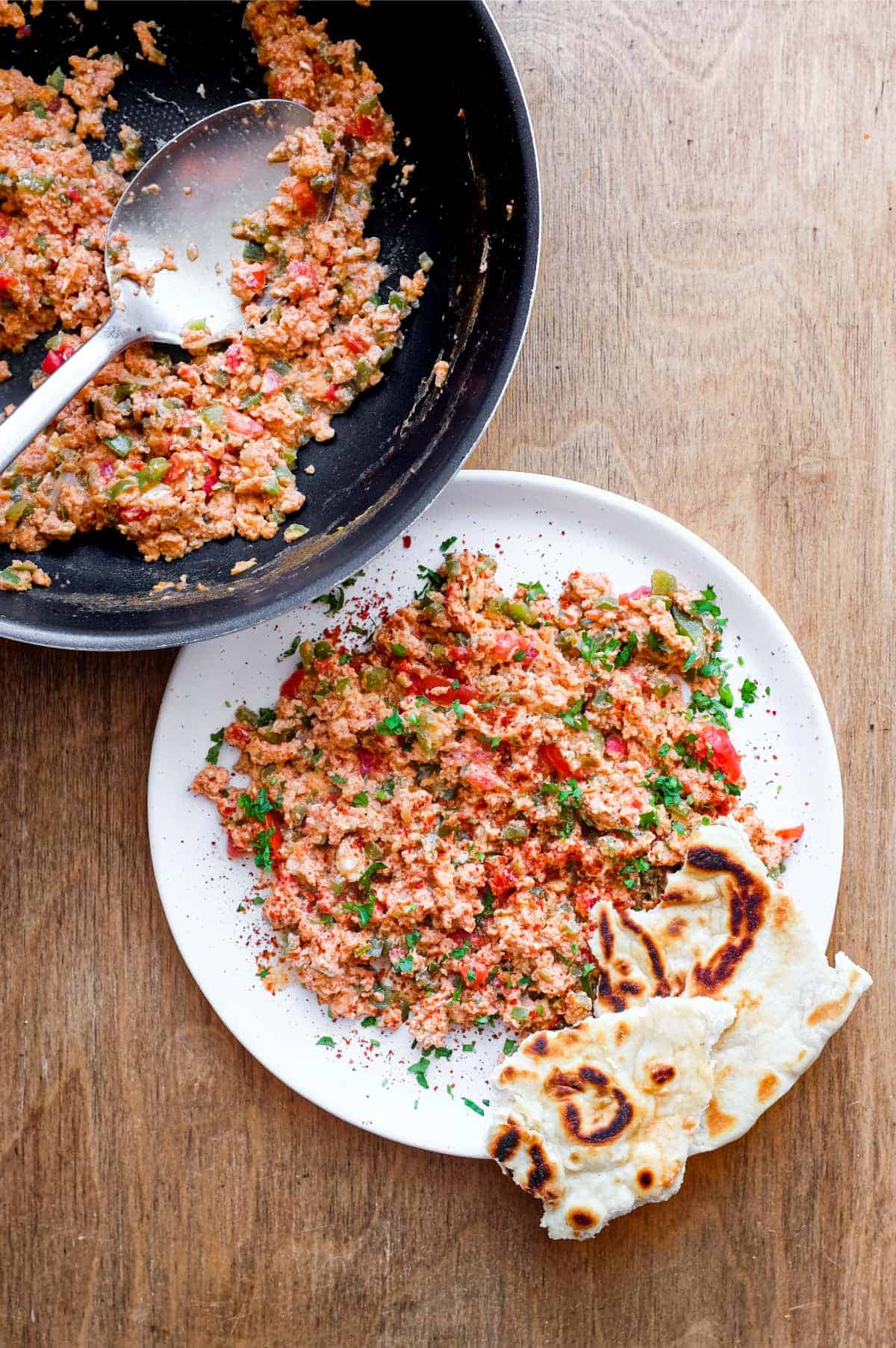 A pan of Turkish menemen alongside a plate with a portion of eggs