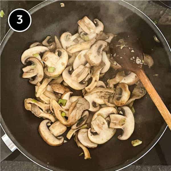 Mushrooms sautéing in a wok with a wooden spoon
