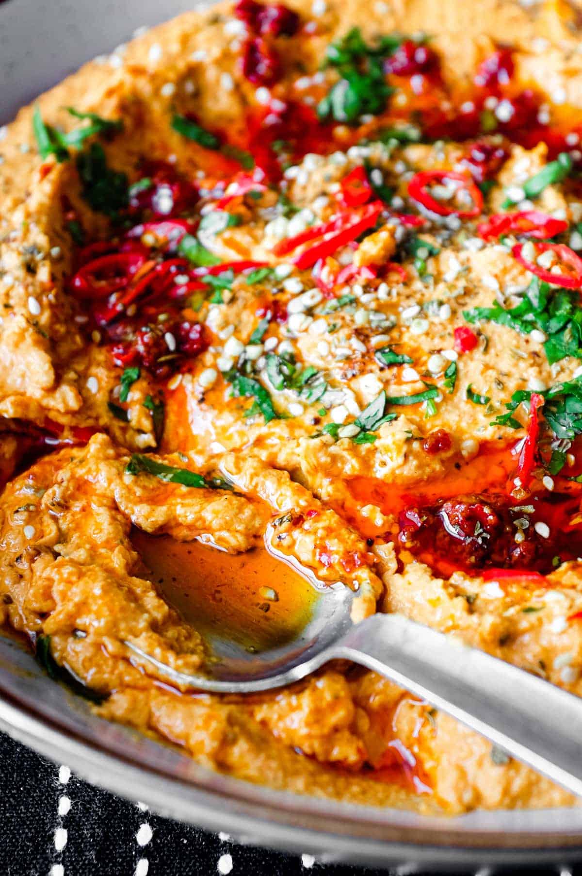 A bowl of Harissa Hummus garnished with chillies, chilli oil, zaatar and fresh cilantro.