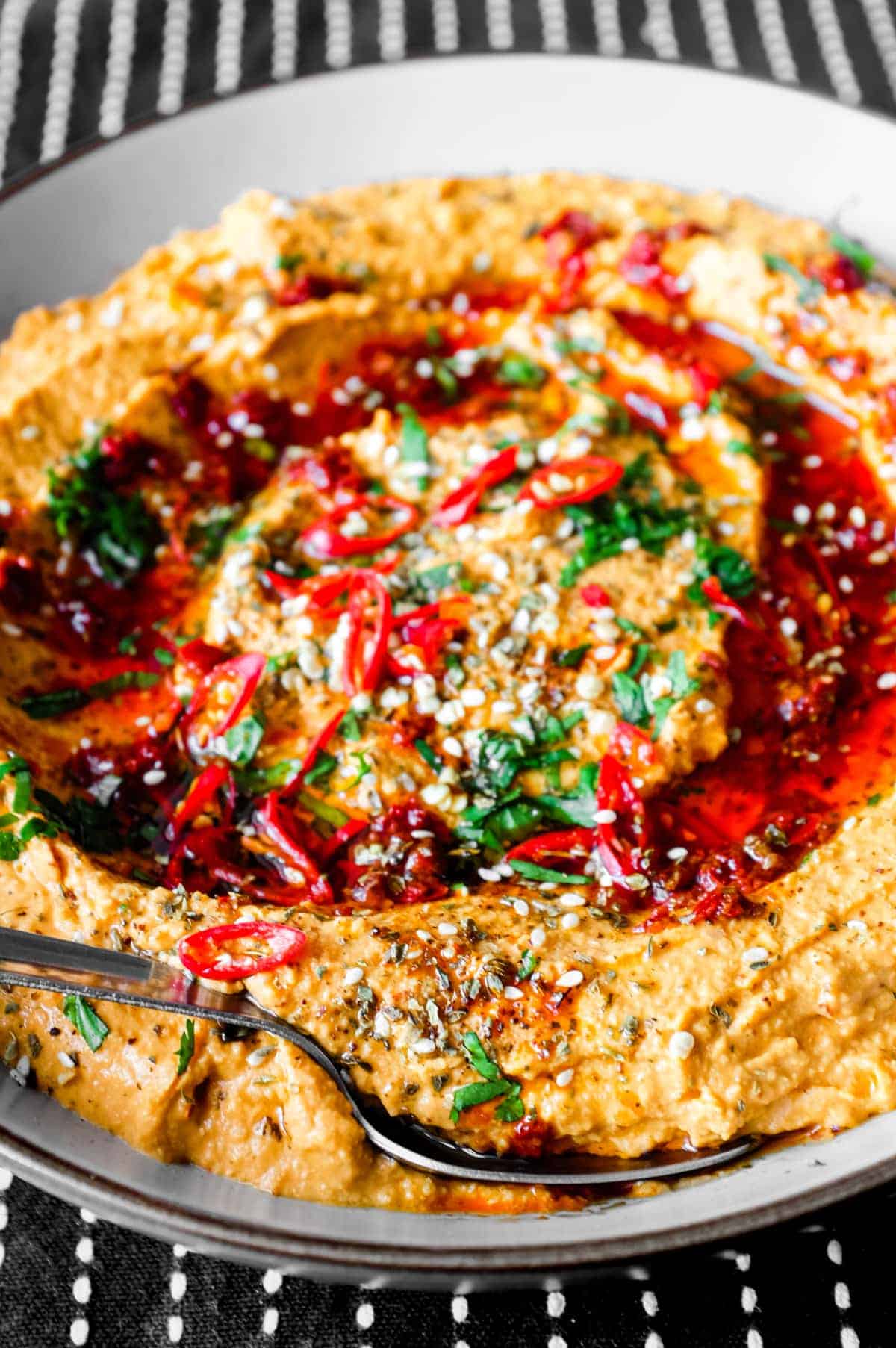 A bowl of Harissa Hummus garnished with chillies, chilli oil, zaatar and fresh cilantro.