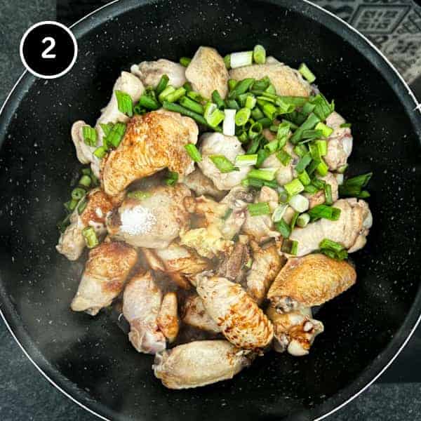 Indonesian chicken wings in a pan with seasonings and spring onion