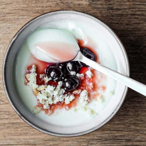 A bowl of lemon cream dessert topped with maraschino cherries and crumbled amaretti biscuits. A spoonful of the cream sits on top.
