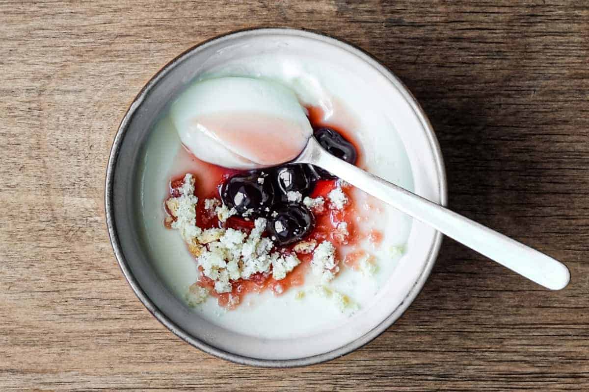 A bowl of lemon cream dessert topped with maraschino cherries and crumbled amaretti biscuits. A spoonful of the cream sits on top.