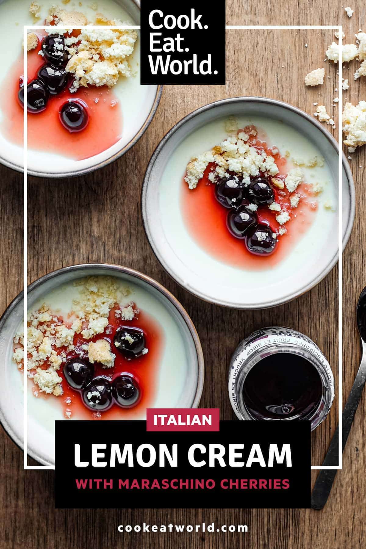 A collection of lemon cream desserts topped with maraschino cherries and crumbled amaretti biscuits. A small jar of Maraschino cherries and a spoon sit alongside. There are a few amaretti crumbs to the right.