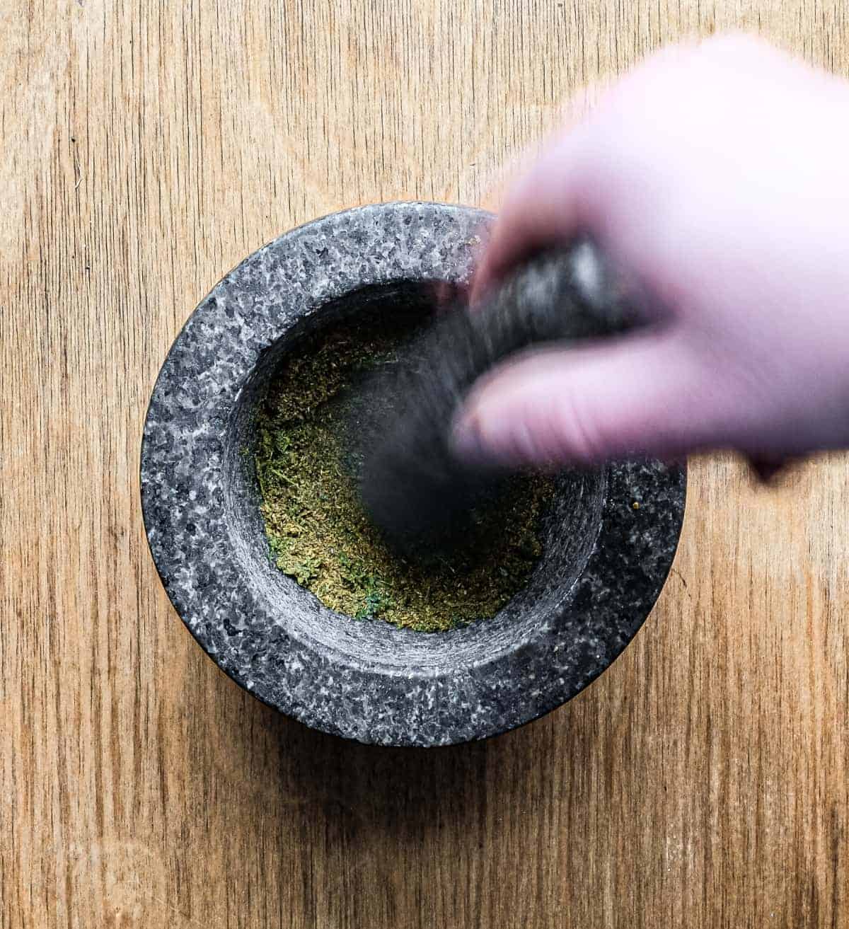 crushing whole spices and fresh curry leaves with a pestle and mortar.
