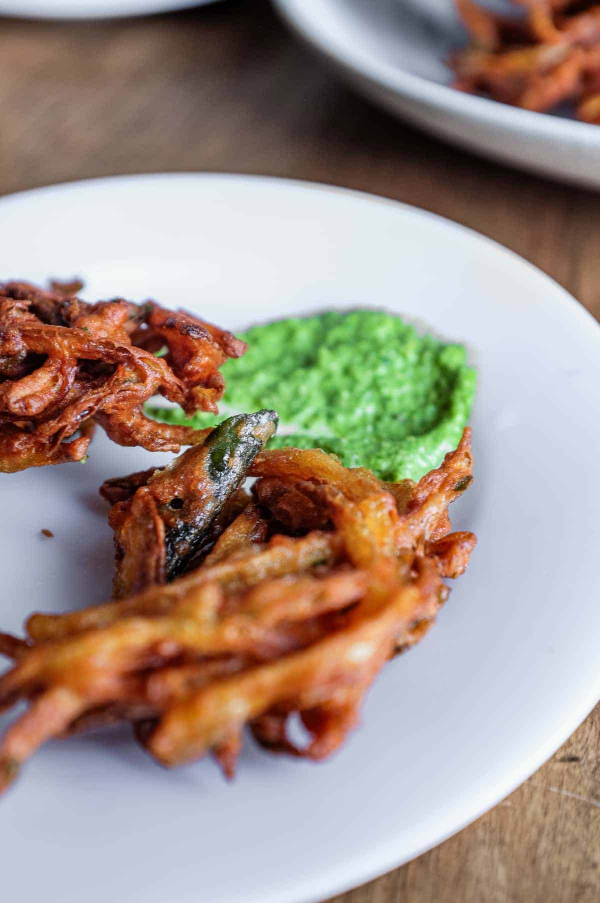 A plate of Indian onion pakoda with a dollop of coriander chutney