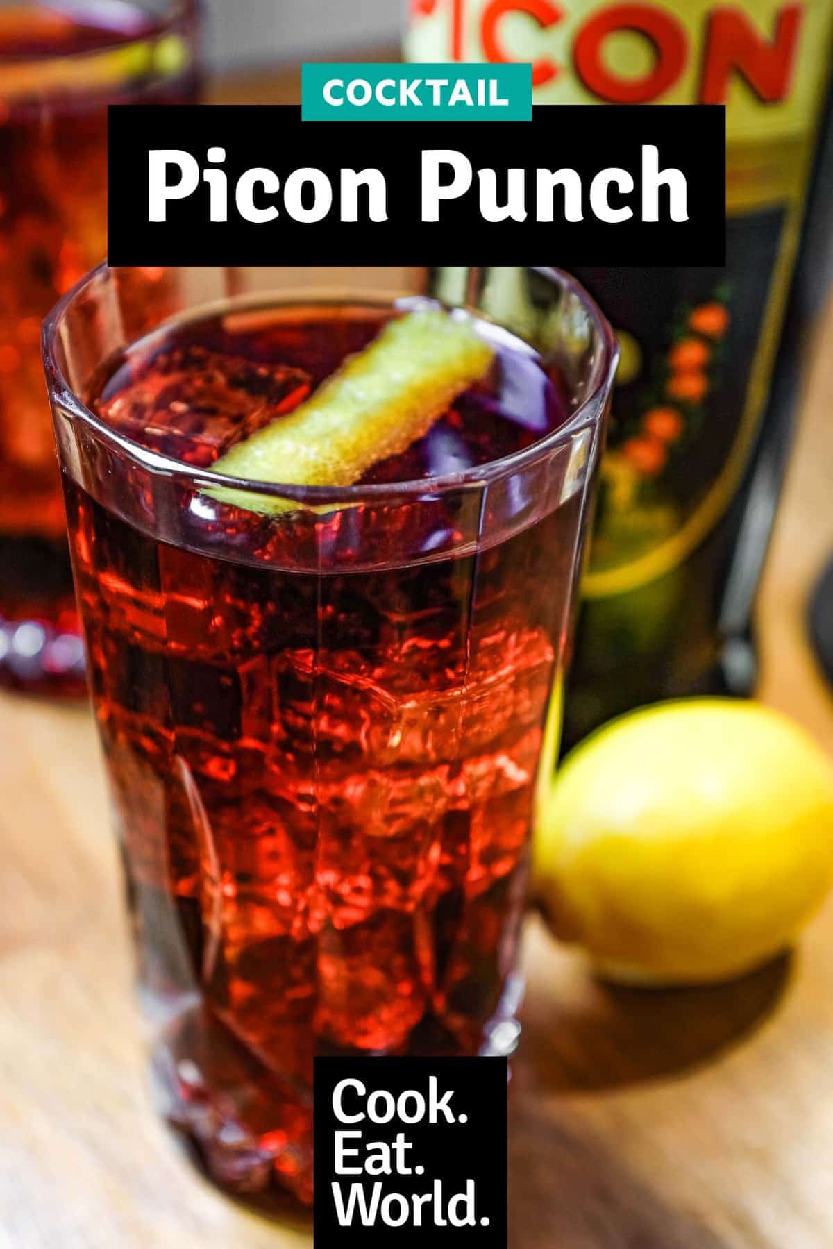 Two cut glass highball glasses of a cocktail called Picon Punch sit alongside a bottle of Picon Amer and a lemon.