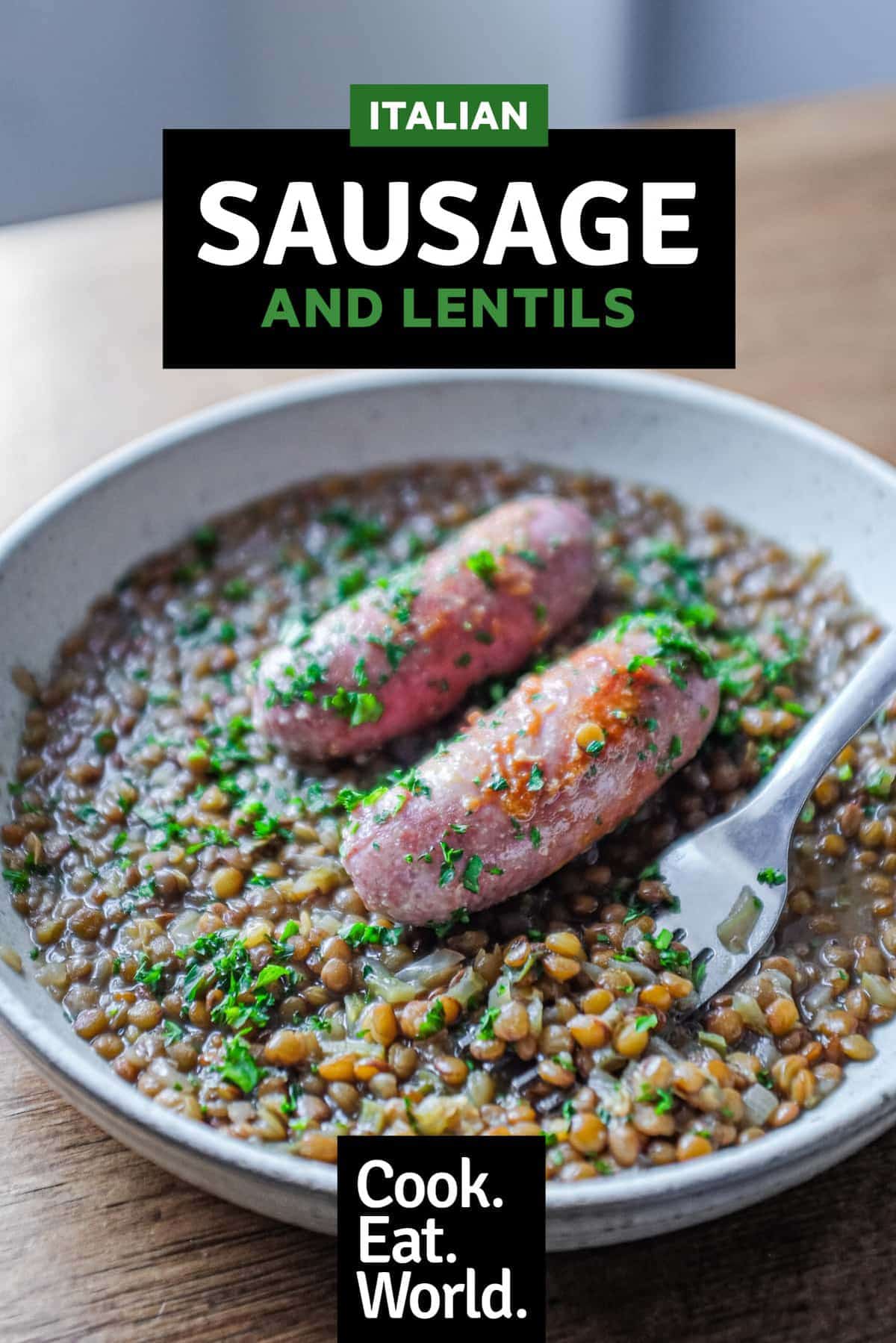 A shallow bowl has a layer of creamy lentils, topped with two Italian pork and fennel sausages. The dish is garnished with fresh parsley.