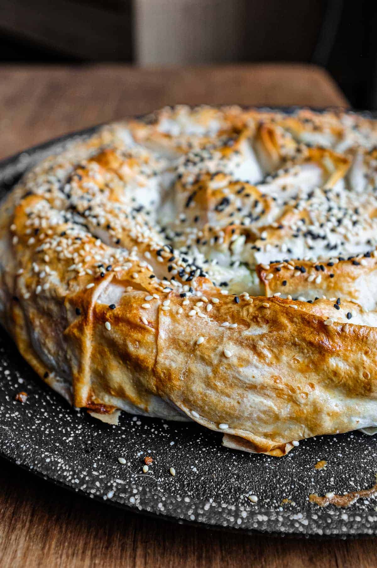 A coiled Turkish Börek on a baking sheet, scattered with sesame and nigella seeds.