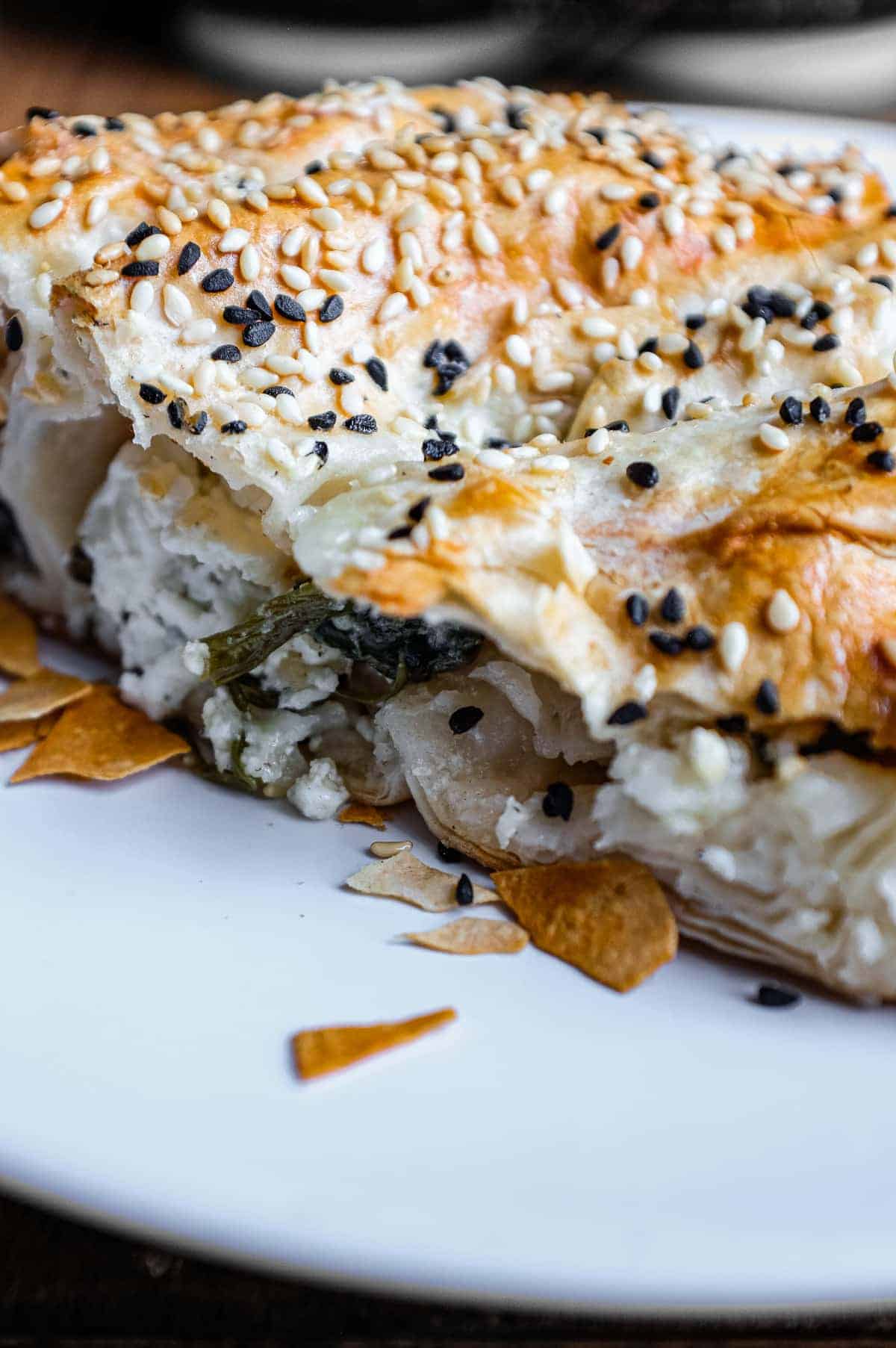 A close up of a Turkish Börek on a baking sheet, scattered with sesame and nigella seeds.