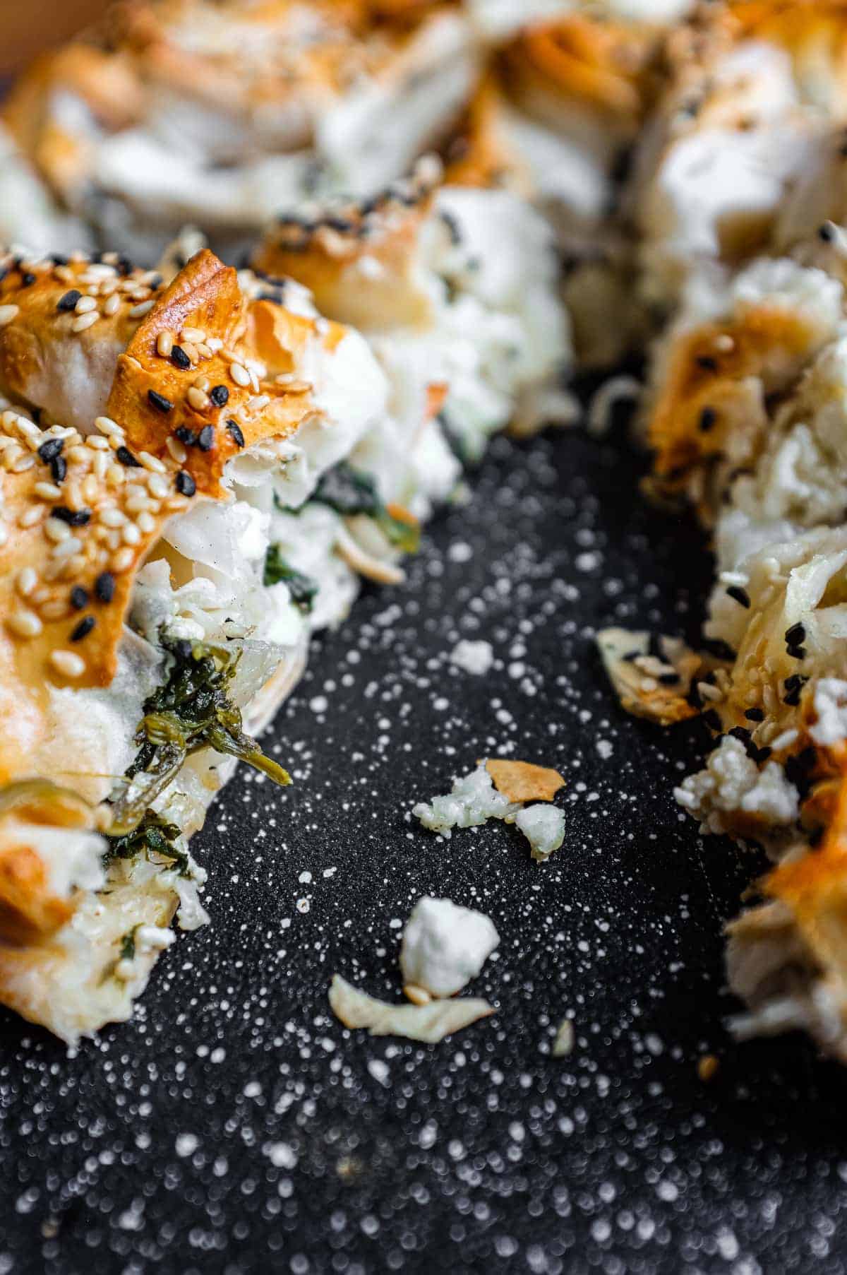A close up of a Turkish Börek on a baking sheet, scattered with sesame and nigella seeds.