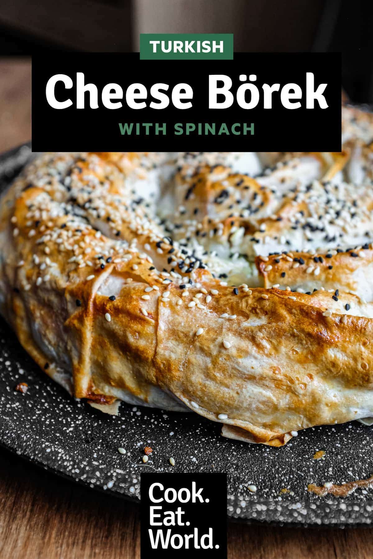A coiled Turkish Börek on a baking sheet, scattered with sesame and nigella seeds.
