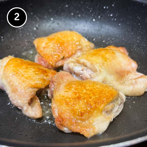 Frying four chicken thighs in a large pan