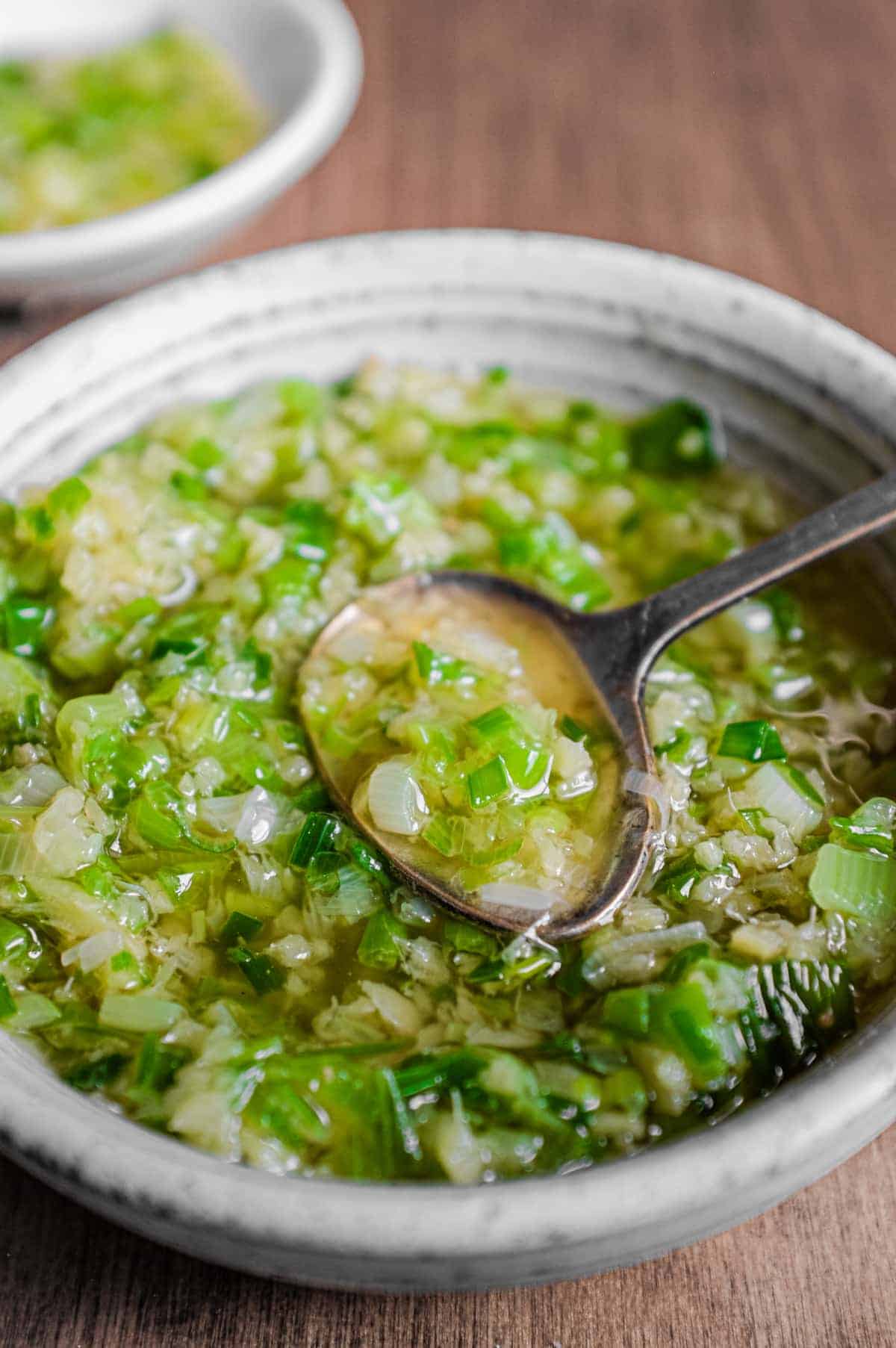 A small bowl of Chinese Ginger Scallion Sauce with a small serving spoon