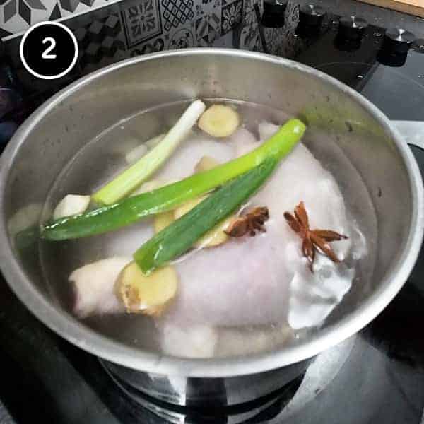 Poaching the chicken portions in a small pan with spring onion, ginger, garlic and star anise.
