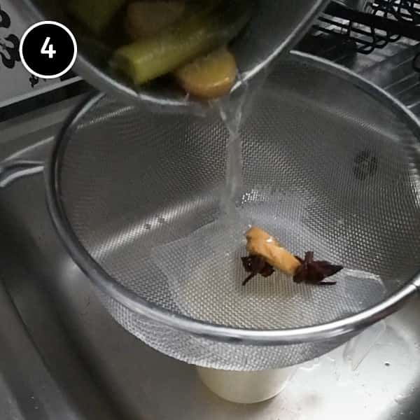 Draining the chicken poaching liquid over a metal sieve into a jug.