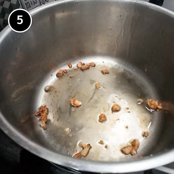 Frying small pieces of chicken skin and fat in a small pan.