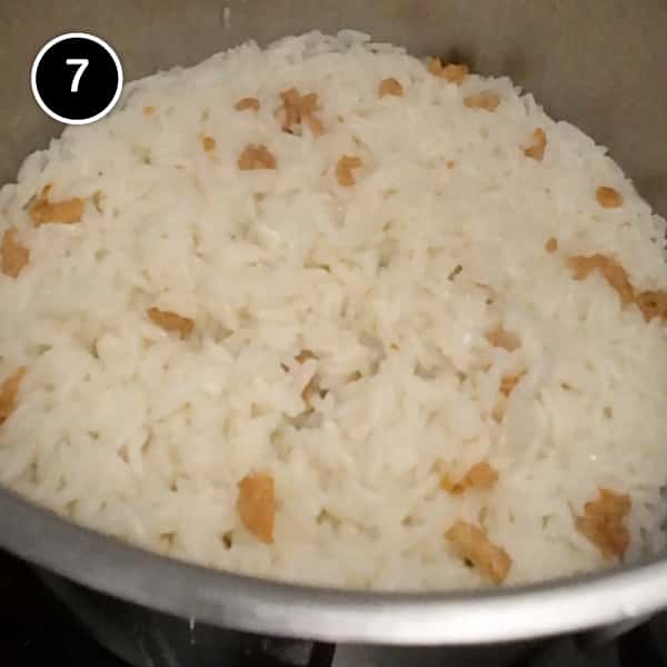 Cooked rice, dotted with small pieces of chicken skin in a small pan.