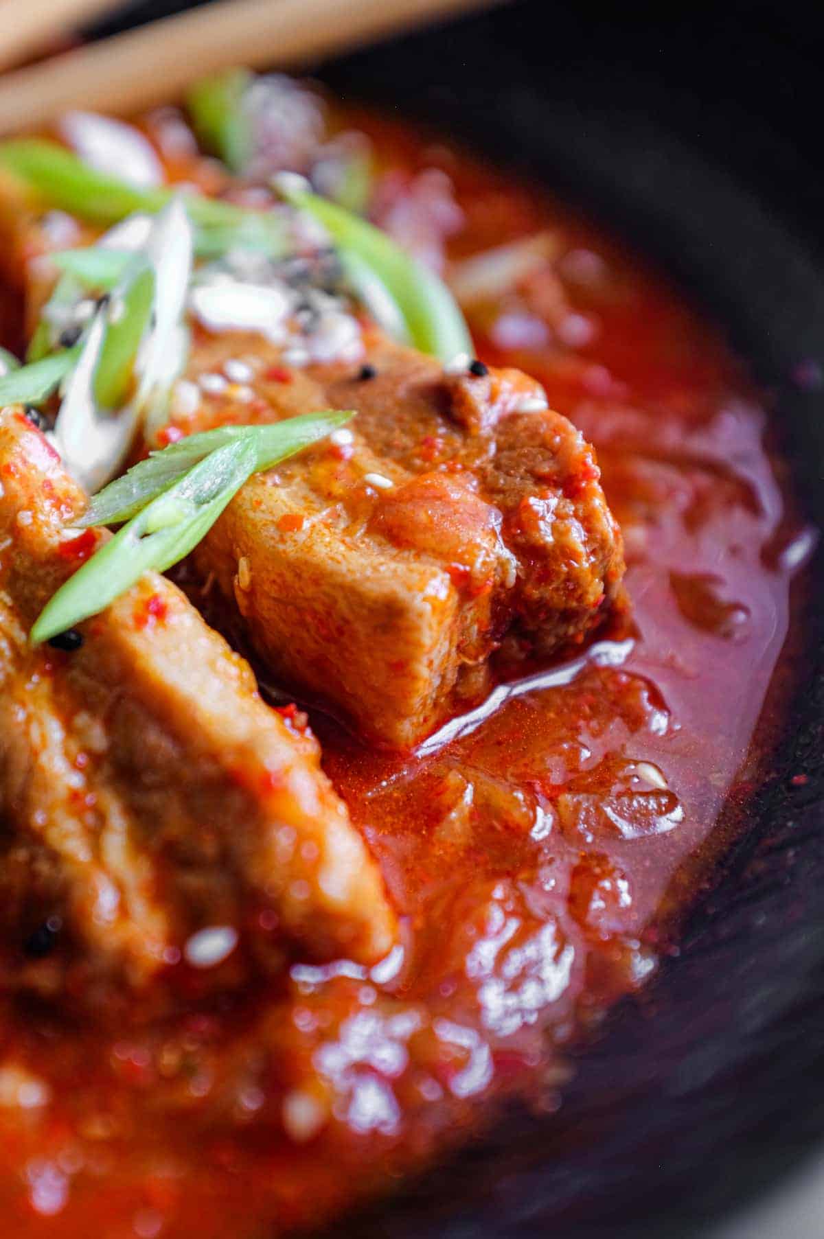 A large black bowl of Kimchi Pork Stew scattered with sesame seeds, nigella seeds and spring onion