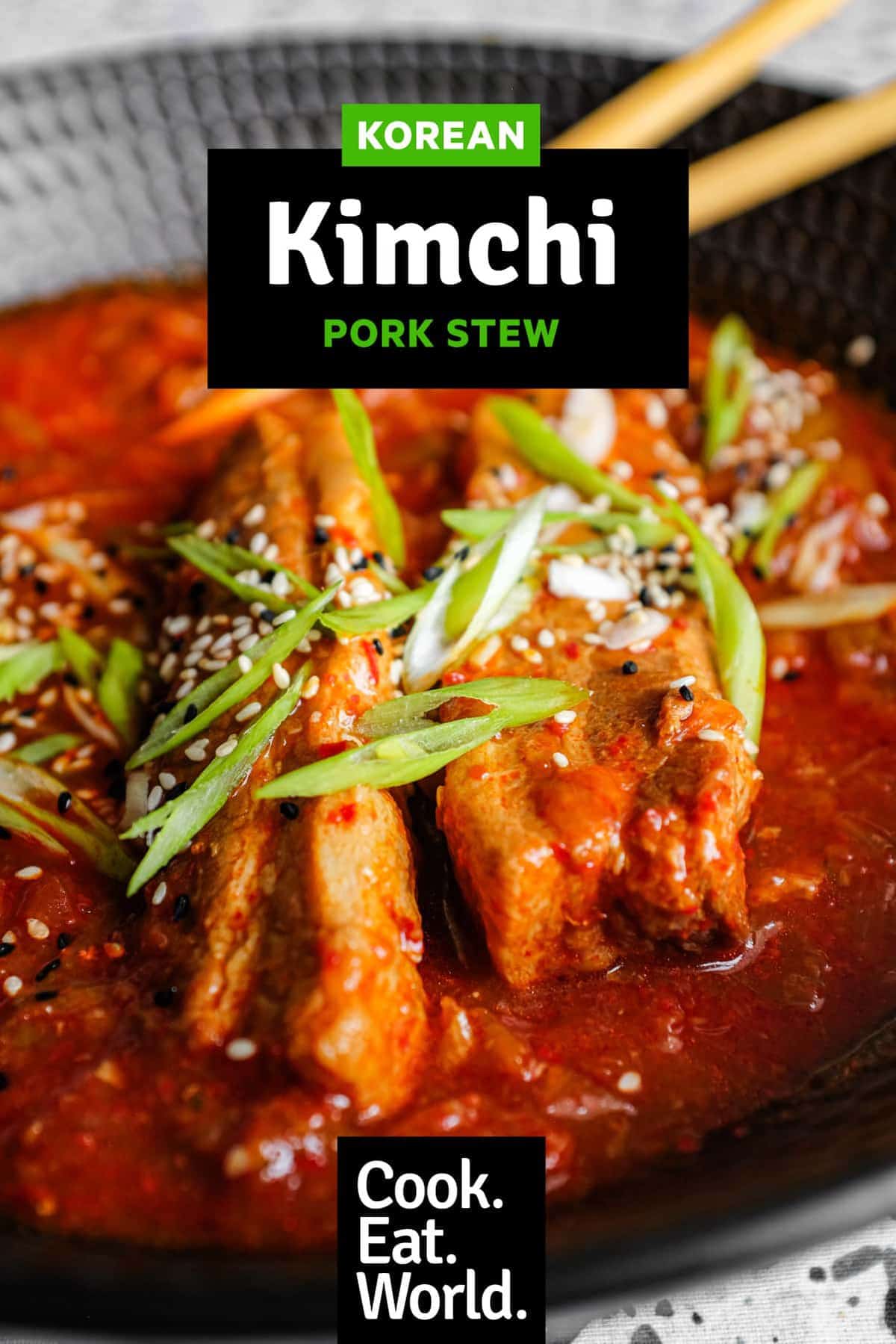 A large black bowl of Kimchi Pork Stew scattered with sesame seeds, nigella seeds and spring onion 