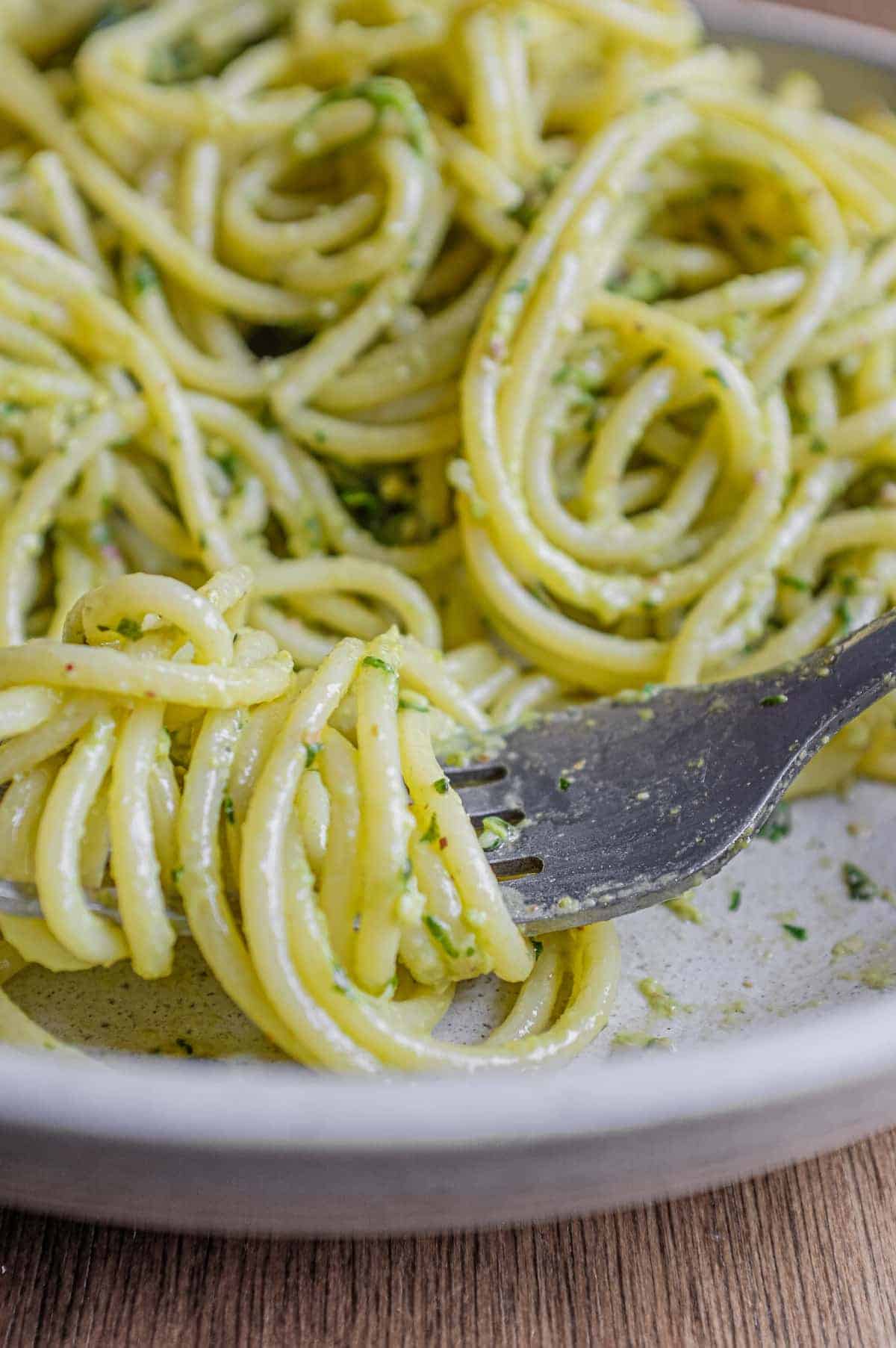 A fork wraps around spaghetti with Pistachio Pesto in a large bowl