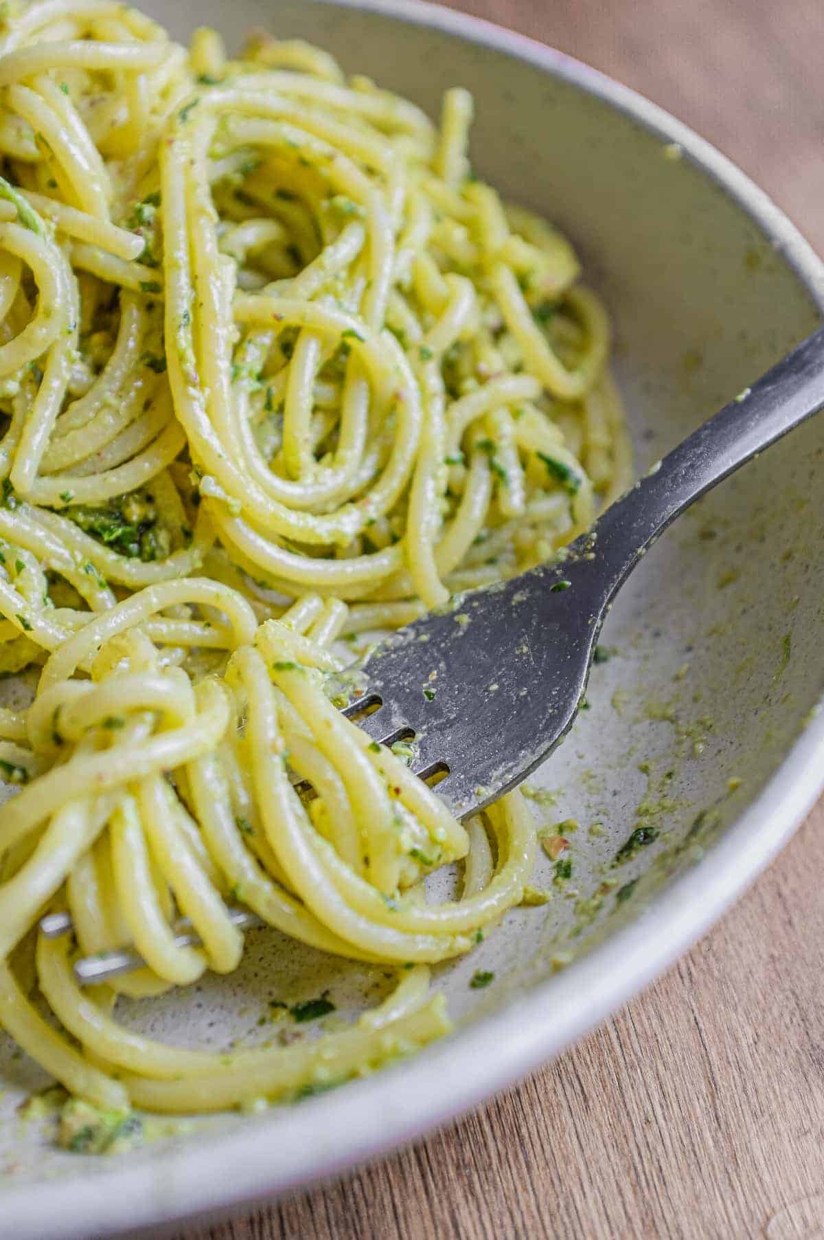 A fork wraps around spaghetti with Pistachio Pesto in a large bowl