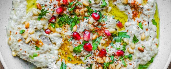 A platter of Baba Ghanoush garnished with parsley, pine nuts and pomegranate seeds