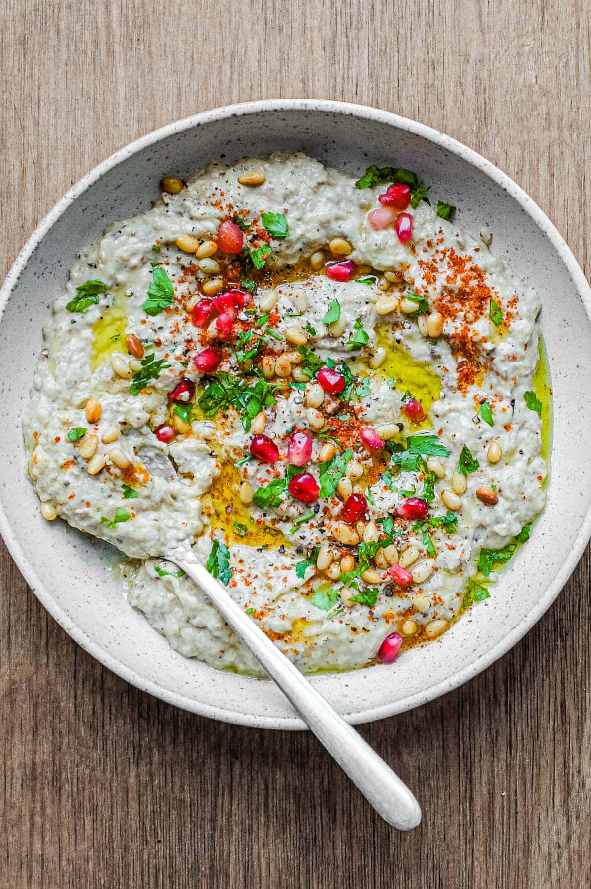 A platter of Baba Ghanoush garnished with parsley, pine nuts and pomegranate seeds