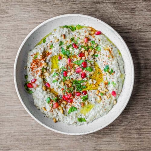 A platter of Baba Ghanoush garnished with parsley, pine nuts and pomegranate seeds