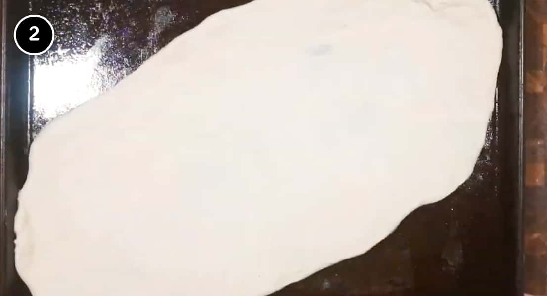 Stretching pide dough into a large oval shape on a baking sheet