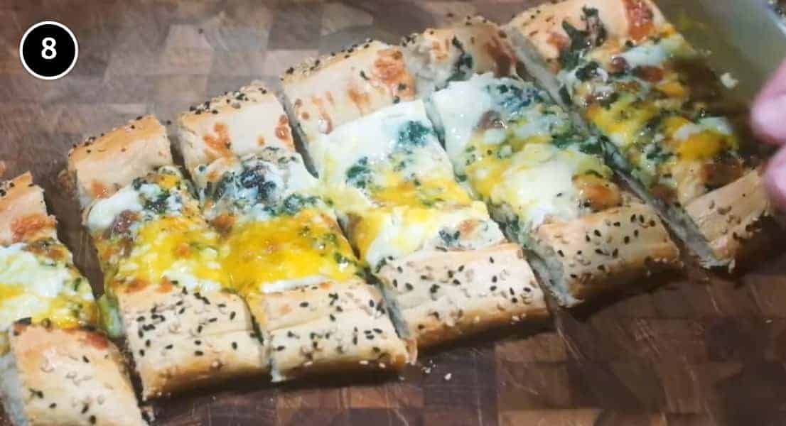 A sliced Turkish Cheese, Egg & Spinach Pide on a wooden board