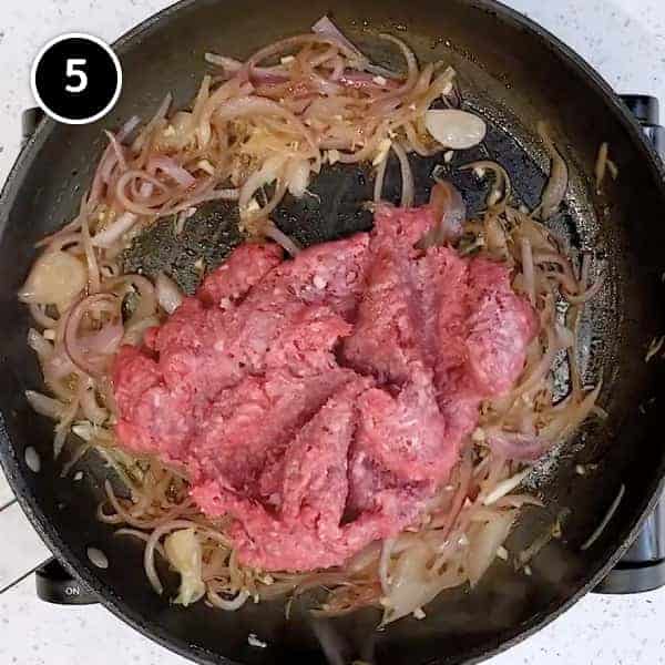 Adding ground lamb to fried onions in a small pan.