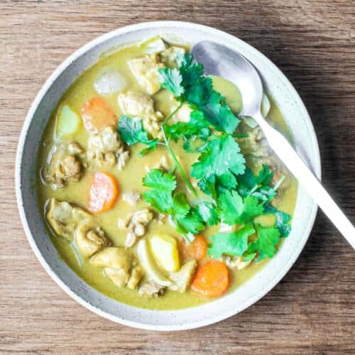 A bowl of Vietnamese chicken curry with chicken, carrots and potatoes. A spoon sits in the sauce.
